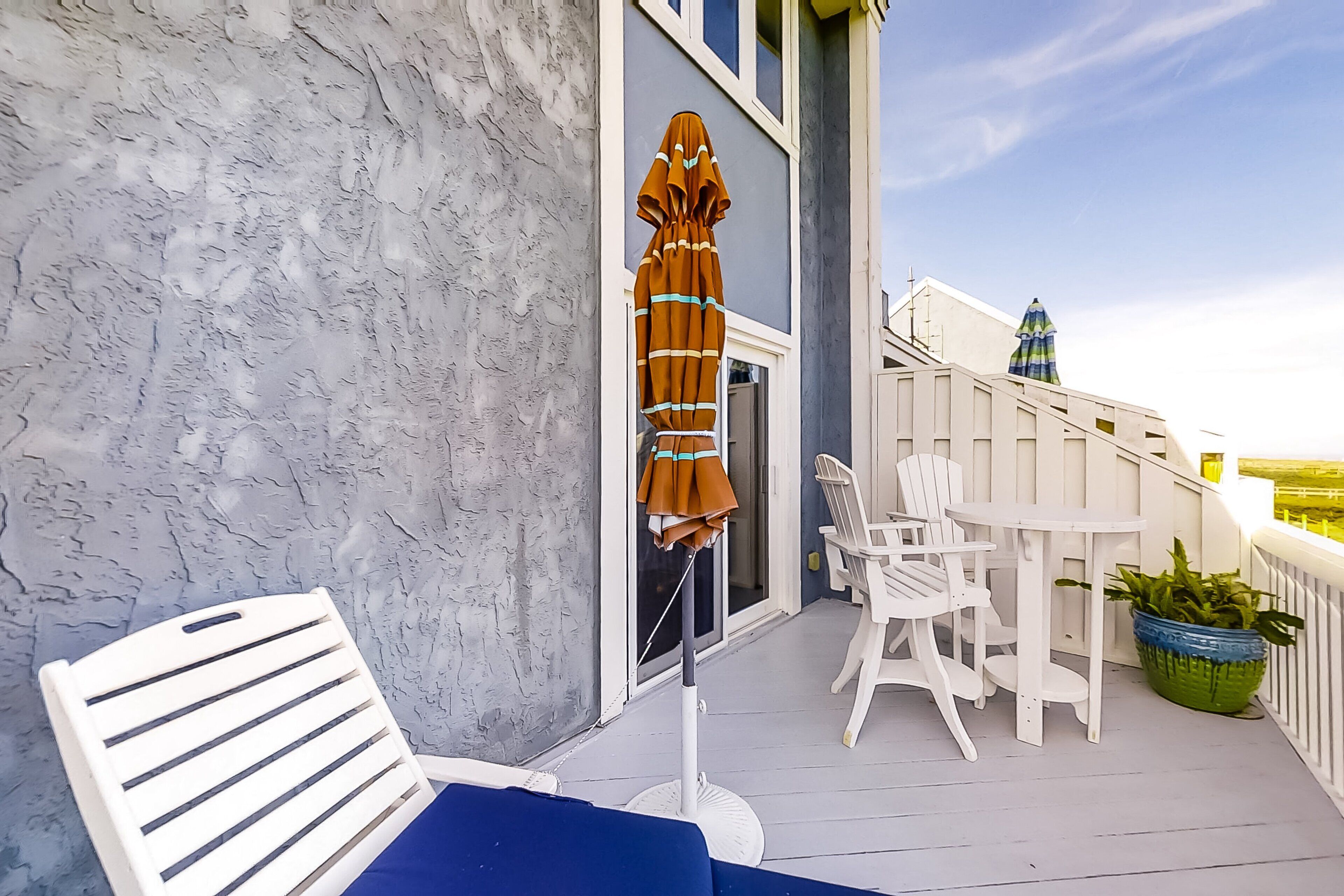 Un balcon avec des chaises blanches, un canapé bleu et un parasol marron.