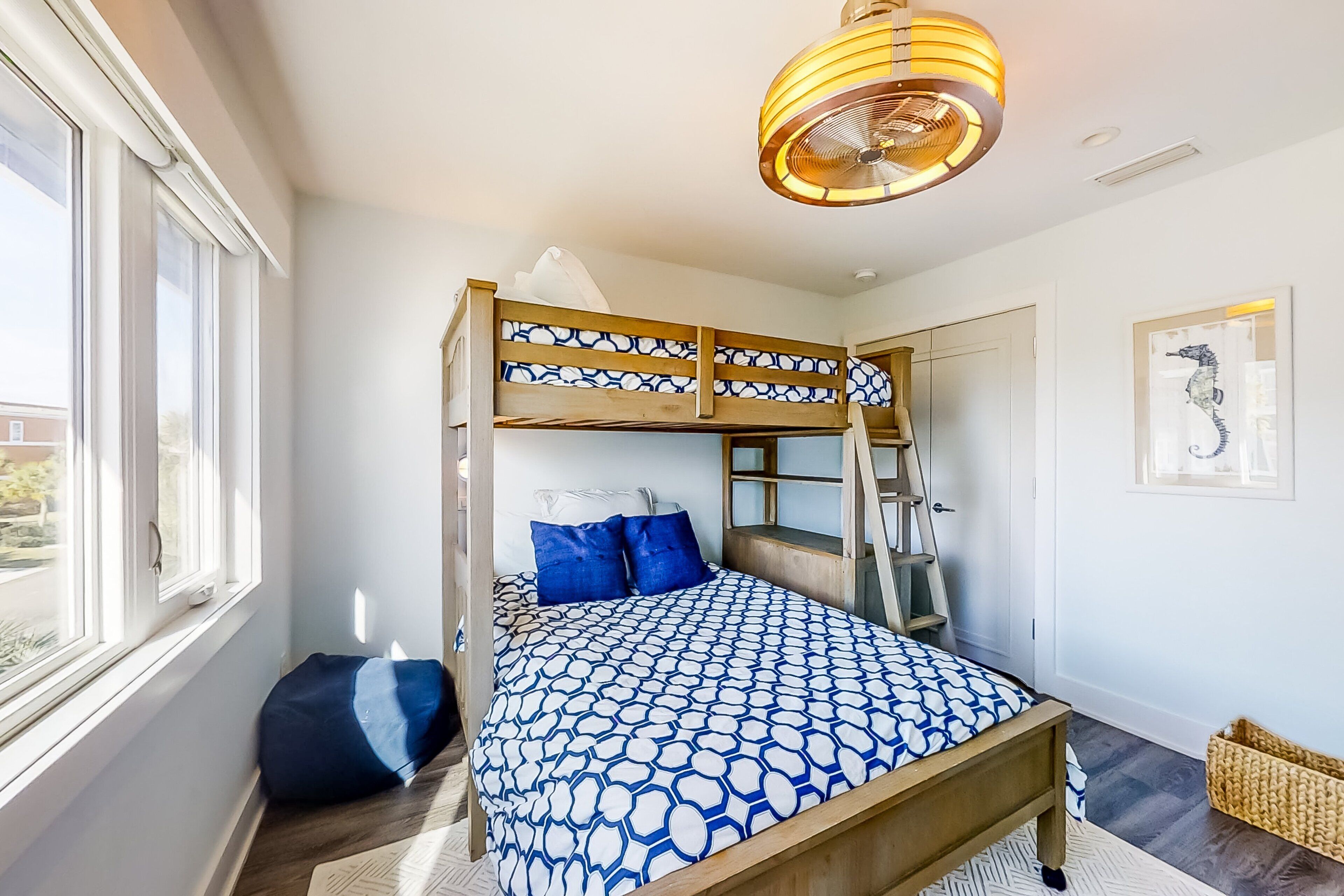 A bunk bed with a patterned bedspread, a ladder, and a window with curtains.