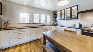 A modern kitchen with white cabinetry, a wooden dining table, and a large window providing natural light. - Oceanfront Townhouse With Ocean Views, Central AC, Wifi, & Outdoor Pool (Fernandina Beach)