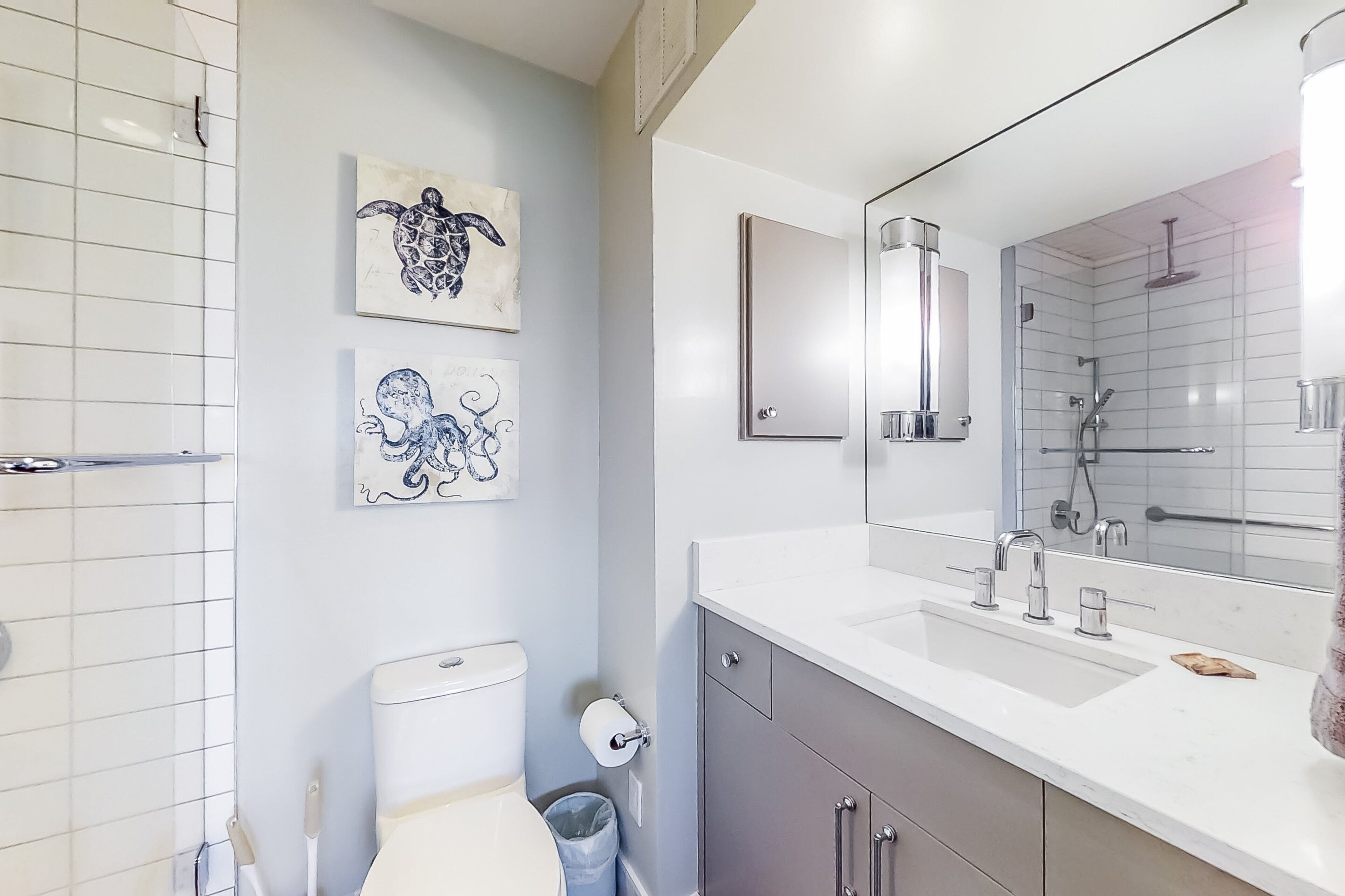 A modern bathroom with a toilet, sink, and shower. There are two wall-mounted artworks depicting sea creatures.