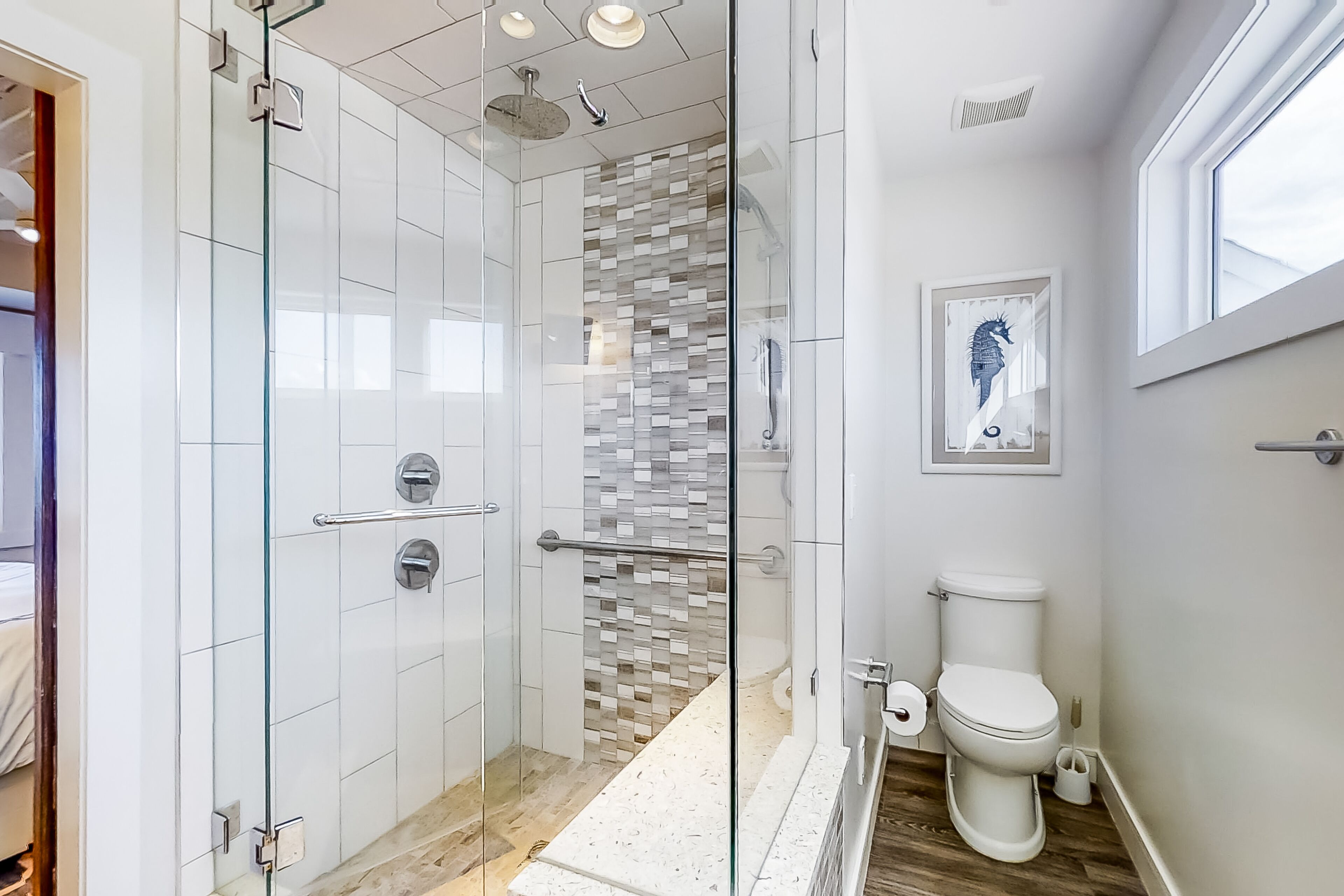 Une salle de bain moderne avec une douche à parois de verre, un mur recouvert de mosaïques, des toilettes et une œuvre d’art encadrée accrochée au mur.