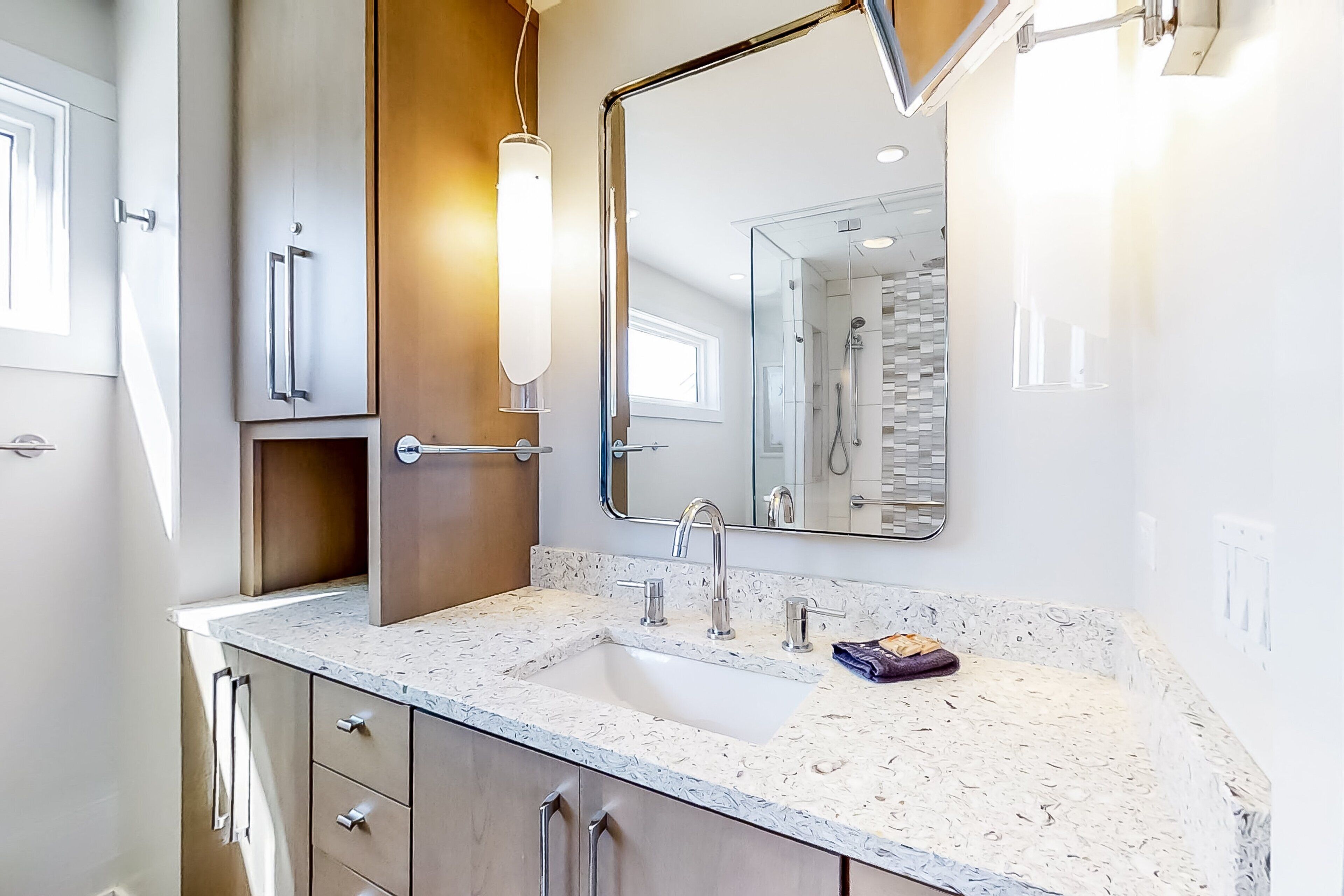 A modern bathroom with a granite countertop, a large mirror, and a shower area.