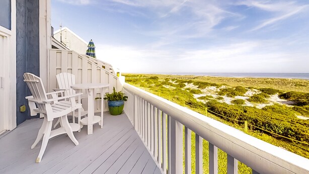 A balcony with white chairs and a table, overlooking a beach with sand dunes. - Oceanfront Townhouse With Ocean Views, Central AC, Wifi, & Outdoor Pool (Fernandina Beach)