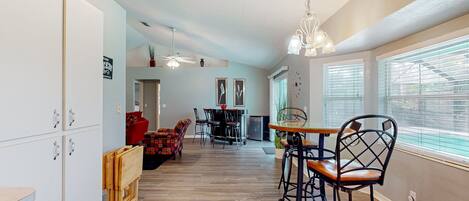 A spacious kitchen with wooden cabinets, a dining area with a table and chairs, and a view through large windows.