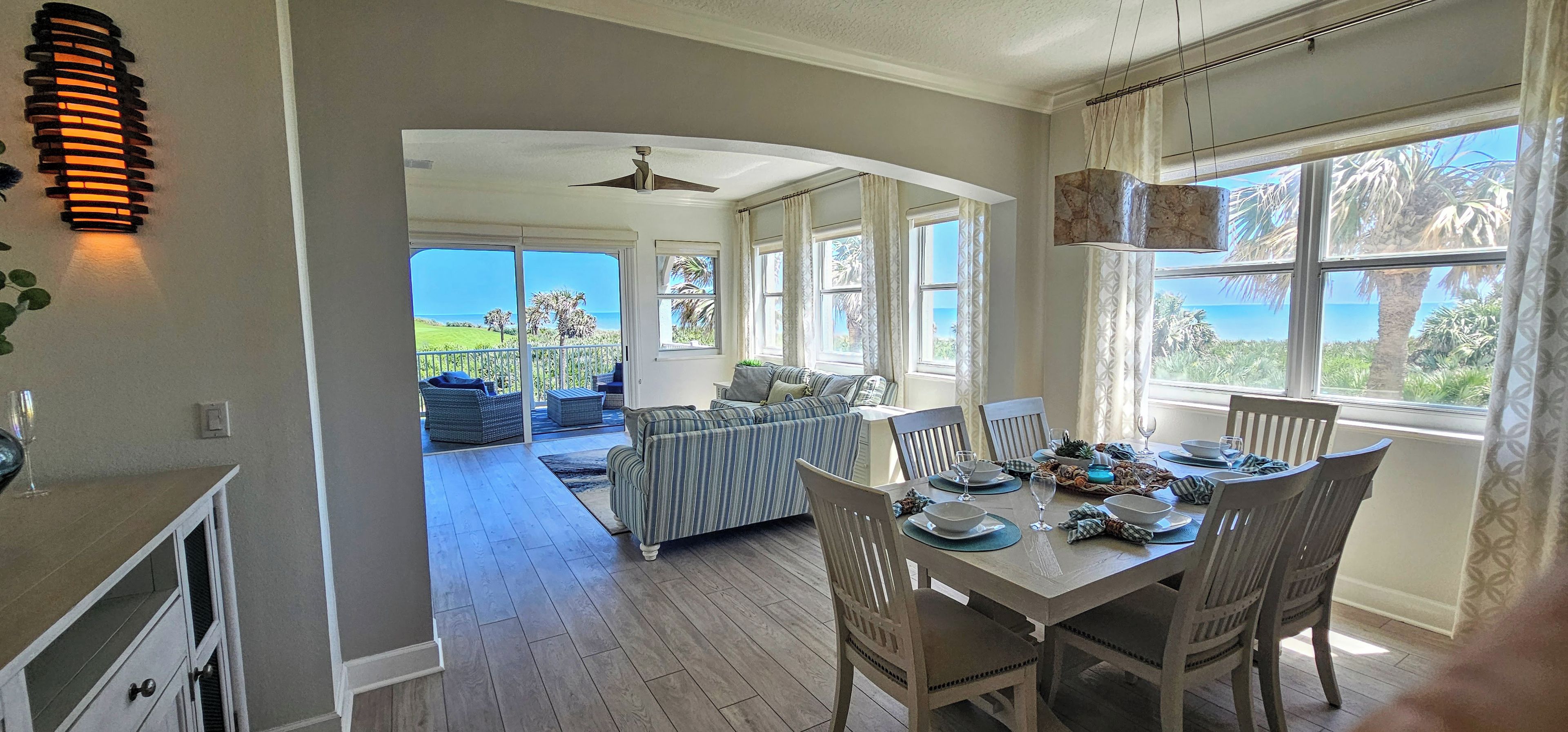 A spacious dining area with a view of the ocean, a ceiling fan, and a dining table set for four.