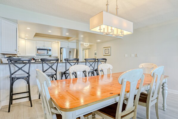 A modern kitchen with white cabinets, stainless steel appliances, and a wooden dining table with white chairs. - Oceanfront Condo With Beach Access, Patio, Outdoor Pools, Tennis Court, W/d, AC (St. Augustine)