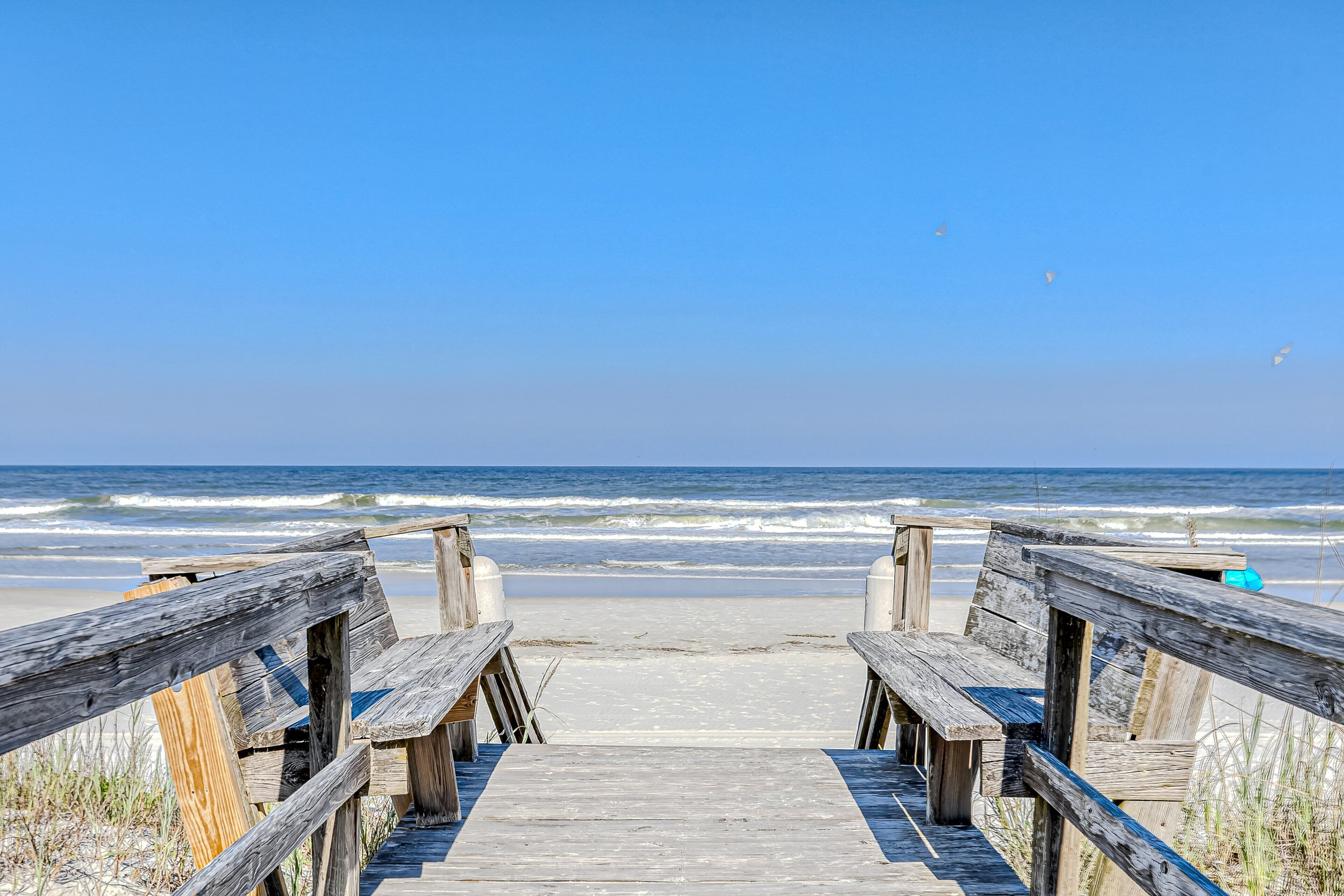A wooden boardwalk leading to the beach with waves in the background.