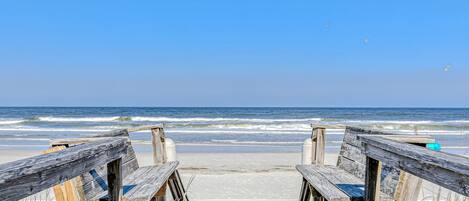 A wooden boardwalk leading to the beach with waves in the background.