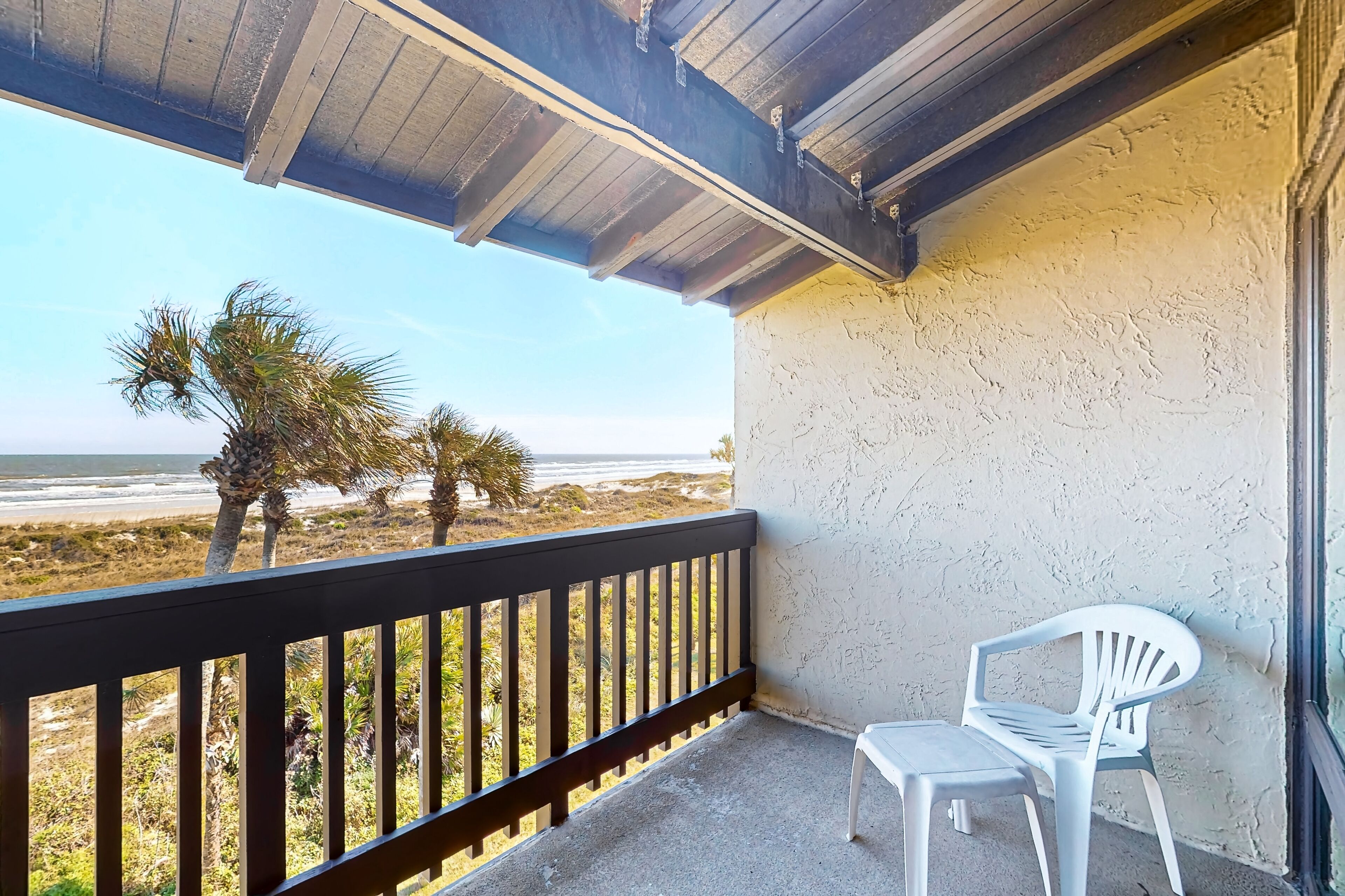A balcony with a view of the beach, a white plastic chair, and a small table.