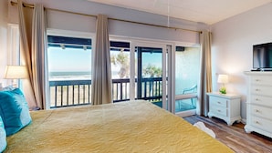 Ein Schlafzimmer mit einem großen Bett, einem Fernseher, einem Nachttisch und Blick auf das Meer durch die Schiebeglastüren.