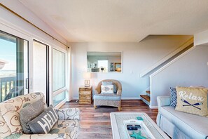 A spacious living room with a large window, a sofa, a chair, and a coffee table. - Oceanfront Condo With Resort Amenities, Beach Access and Pool (St. Augustine)