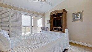 Una camera da letto con un letto, una ventola a soffitto, una TV su un supporto in legno e un balcone con vista.