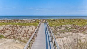 Una passerella di legno che conduce alla spiaggia, circondata da dune sabbiose e vegetazione rada.