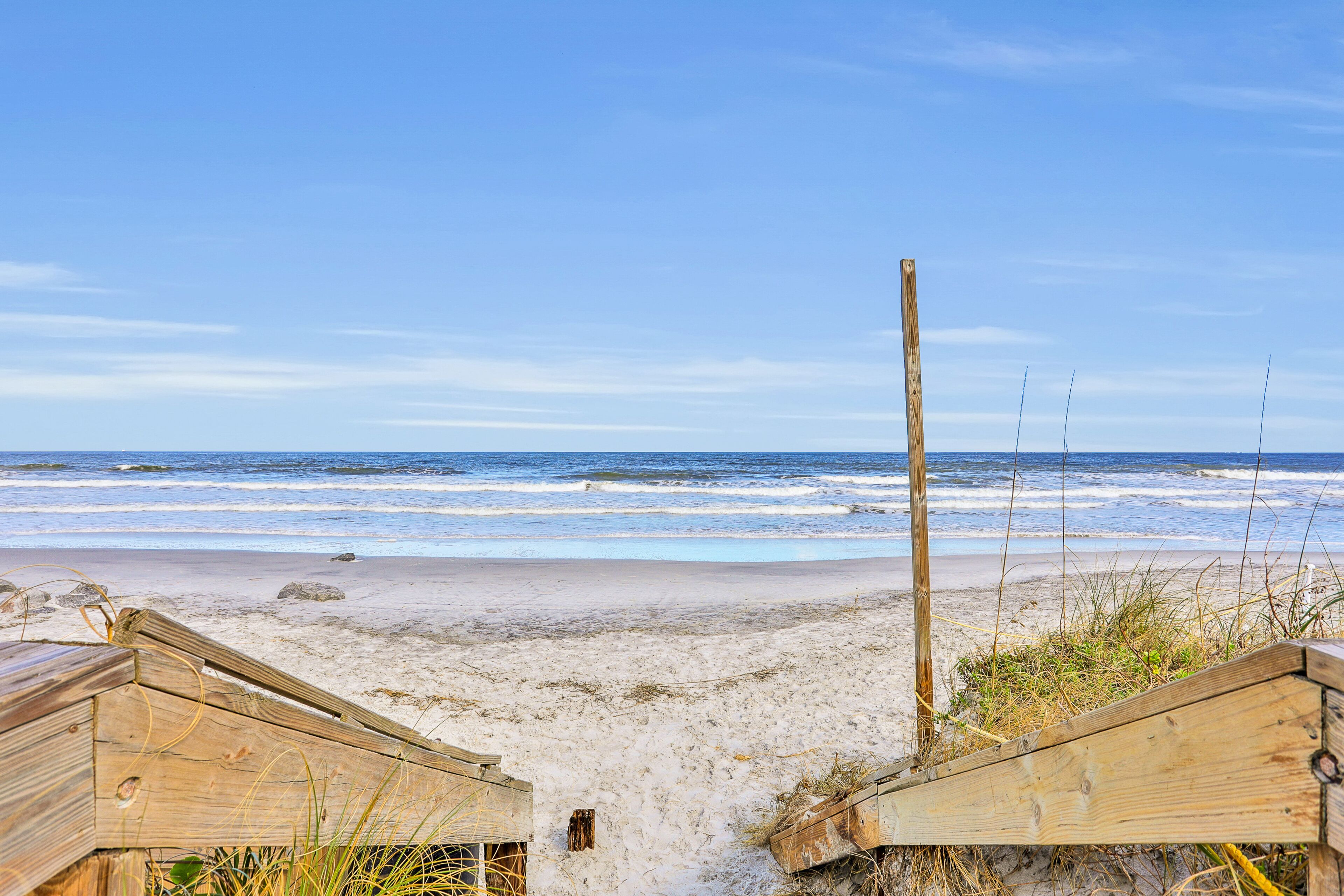 Une promenade en bois qui longe la plage et mène à l’océan, offrant une vue dégagée sur la mer et le ciel.