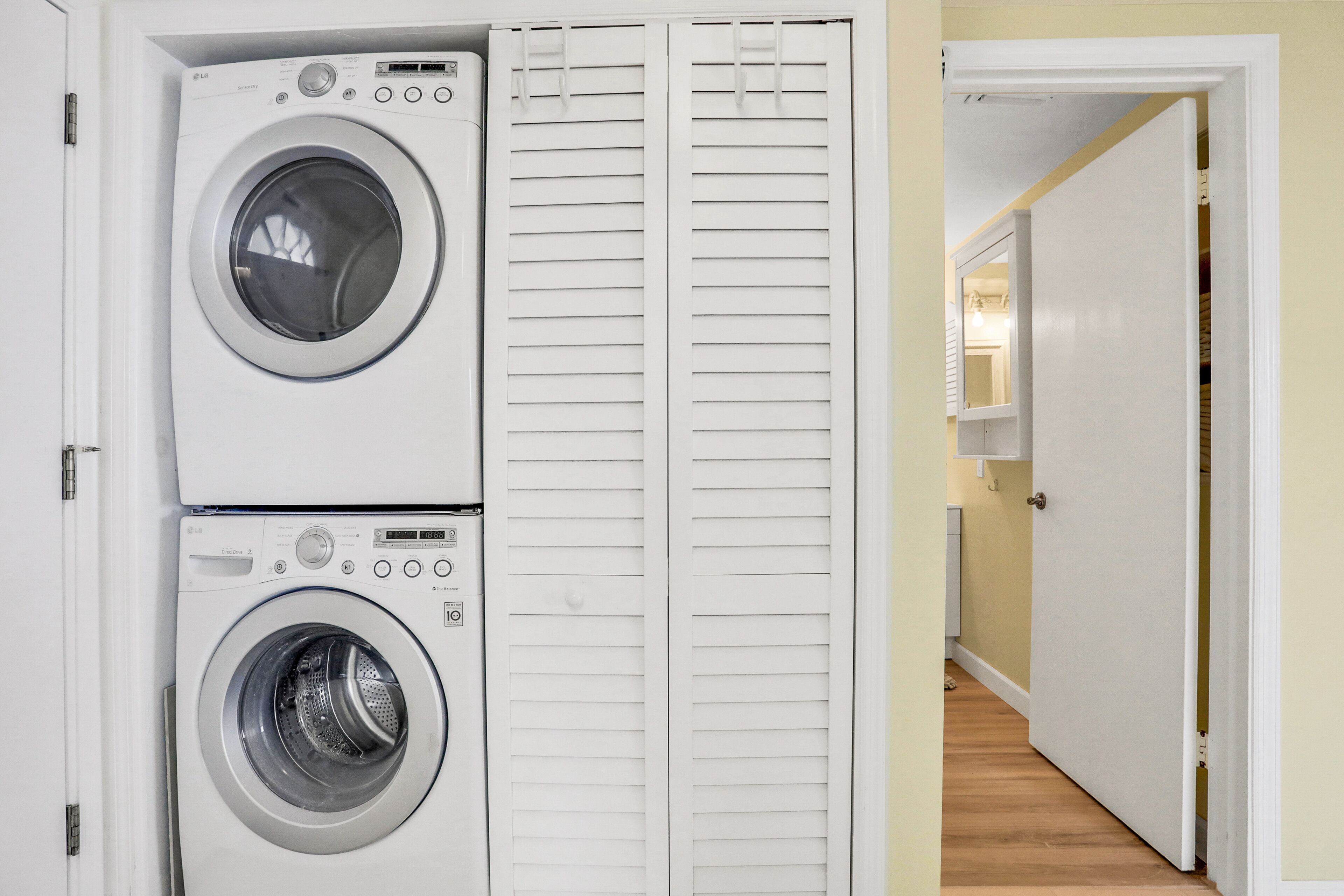 A laundry room with two stacked front-loading washing machines and a white door leading to a hallway.