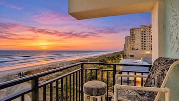 A balcony with a view of the beach and ocean during sunset.