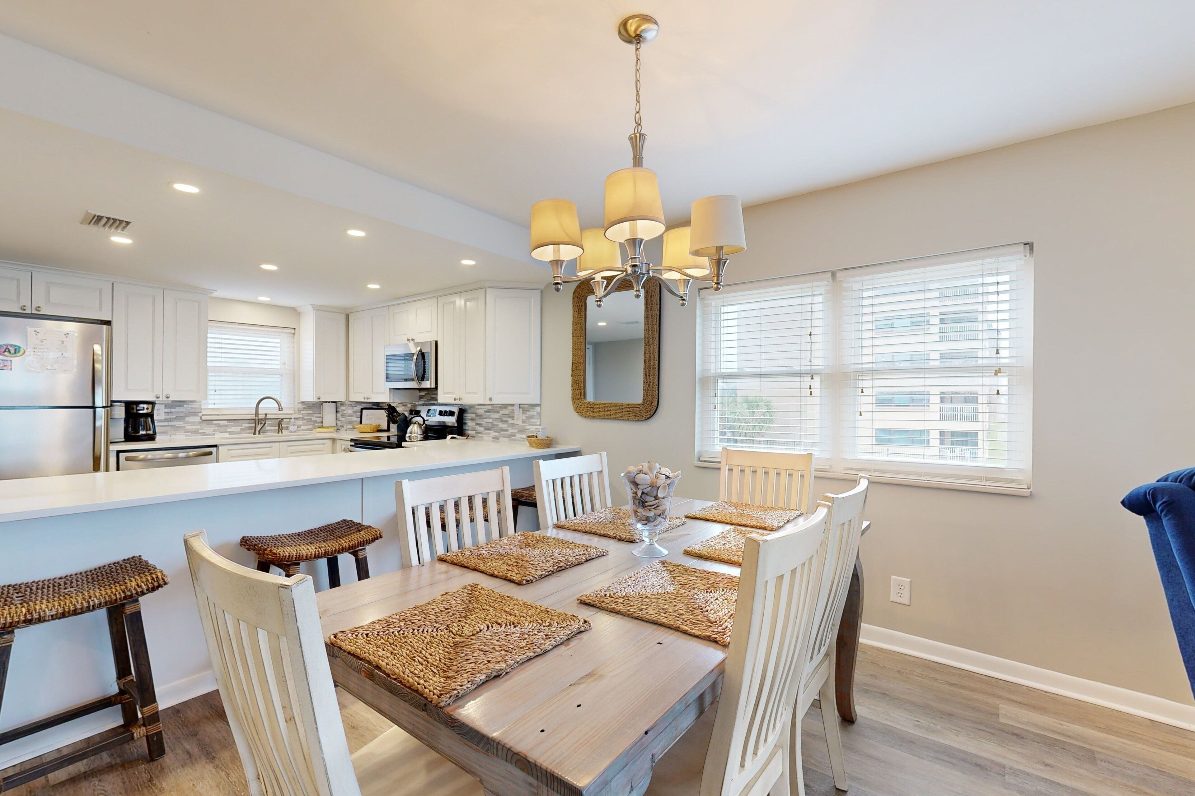 A modern kitchen with white cabinetry, a central island, and a dining area with a wooden table and chairs.