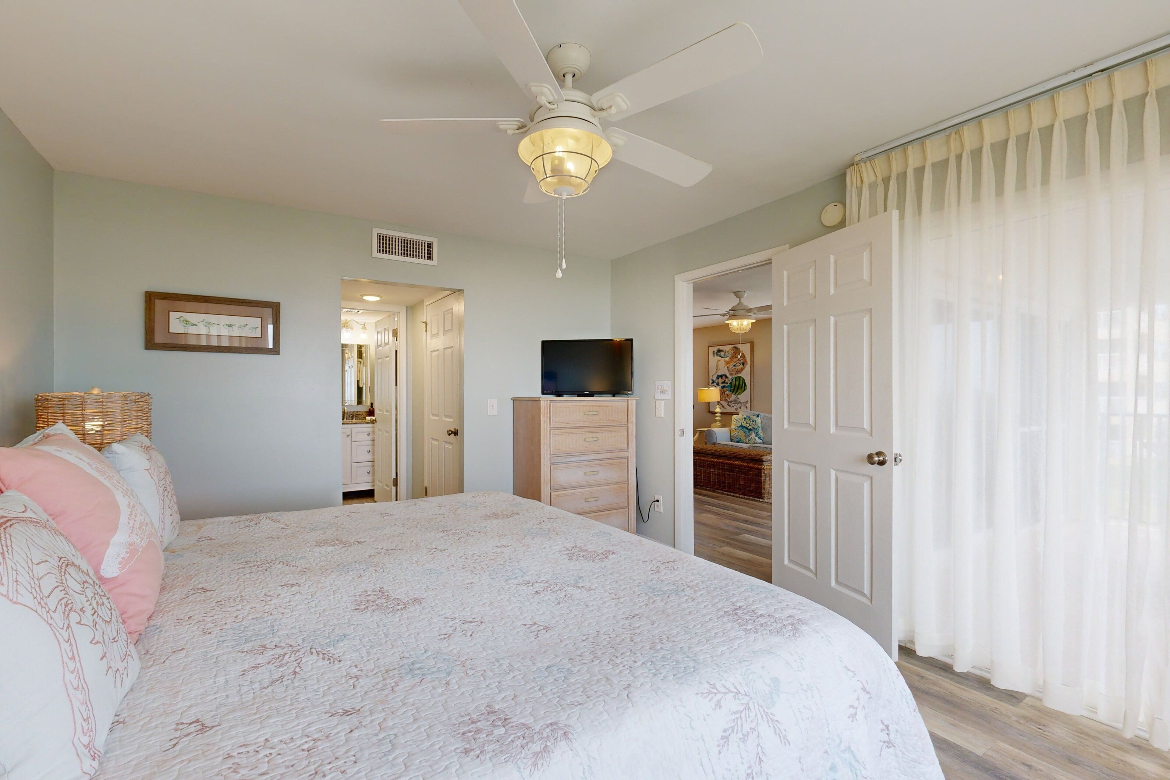 A bedroom with a bed, a ceiling fan, a dresser, and a door leading to another room.