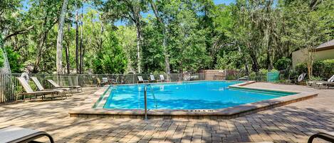 A rectangular swimming pool surrounded by lounge chairs and a brick patio.