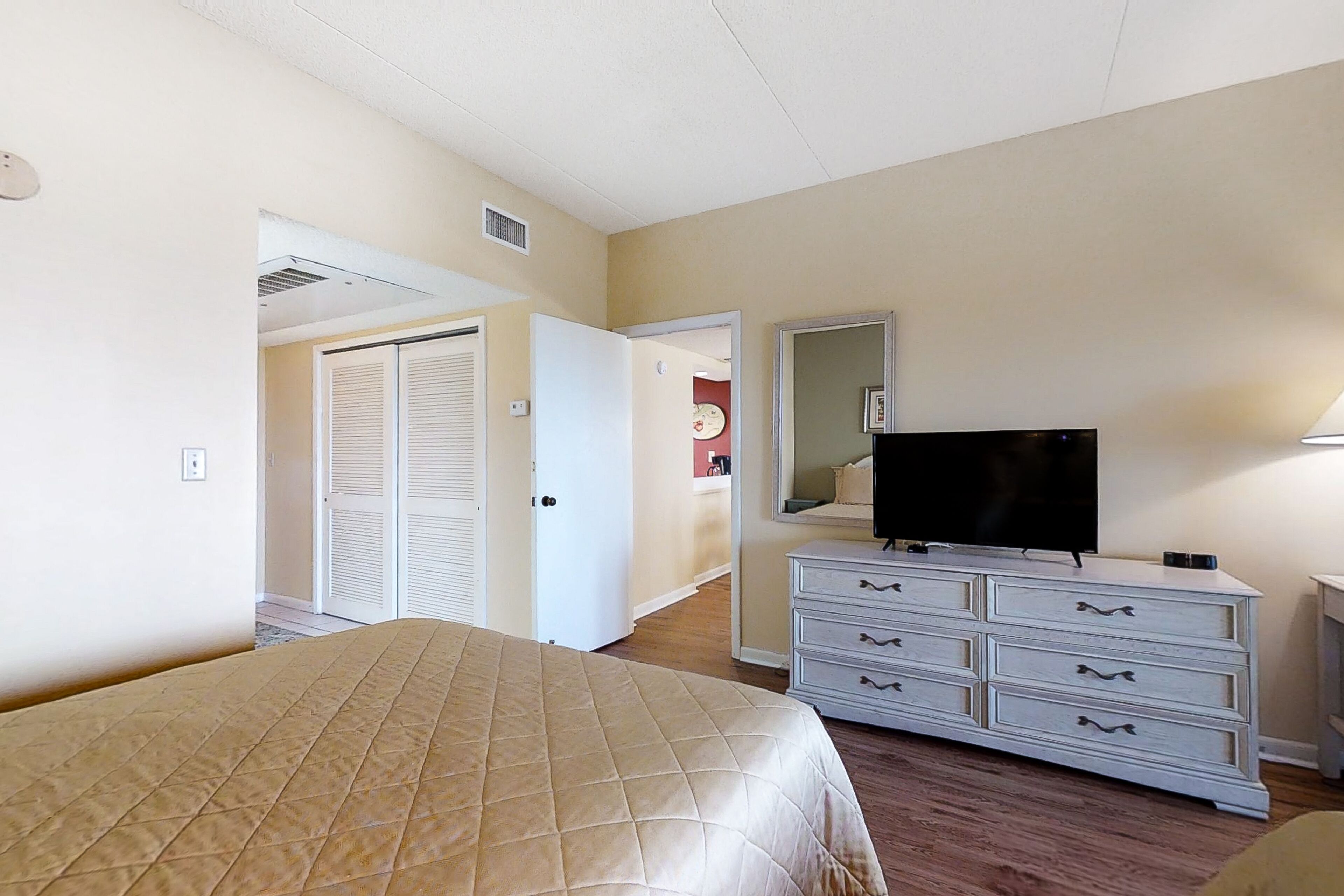 A hotel room with a bed, a dresser, a television, and a door leading to another room.