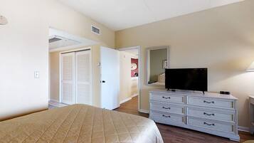 A hotel room with a bed, a dresser, a television, and a door leading to another room.