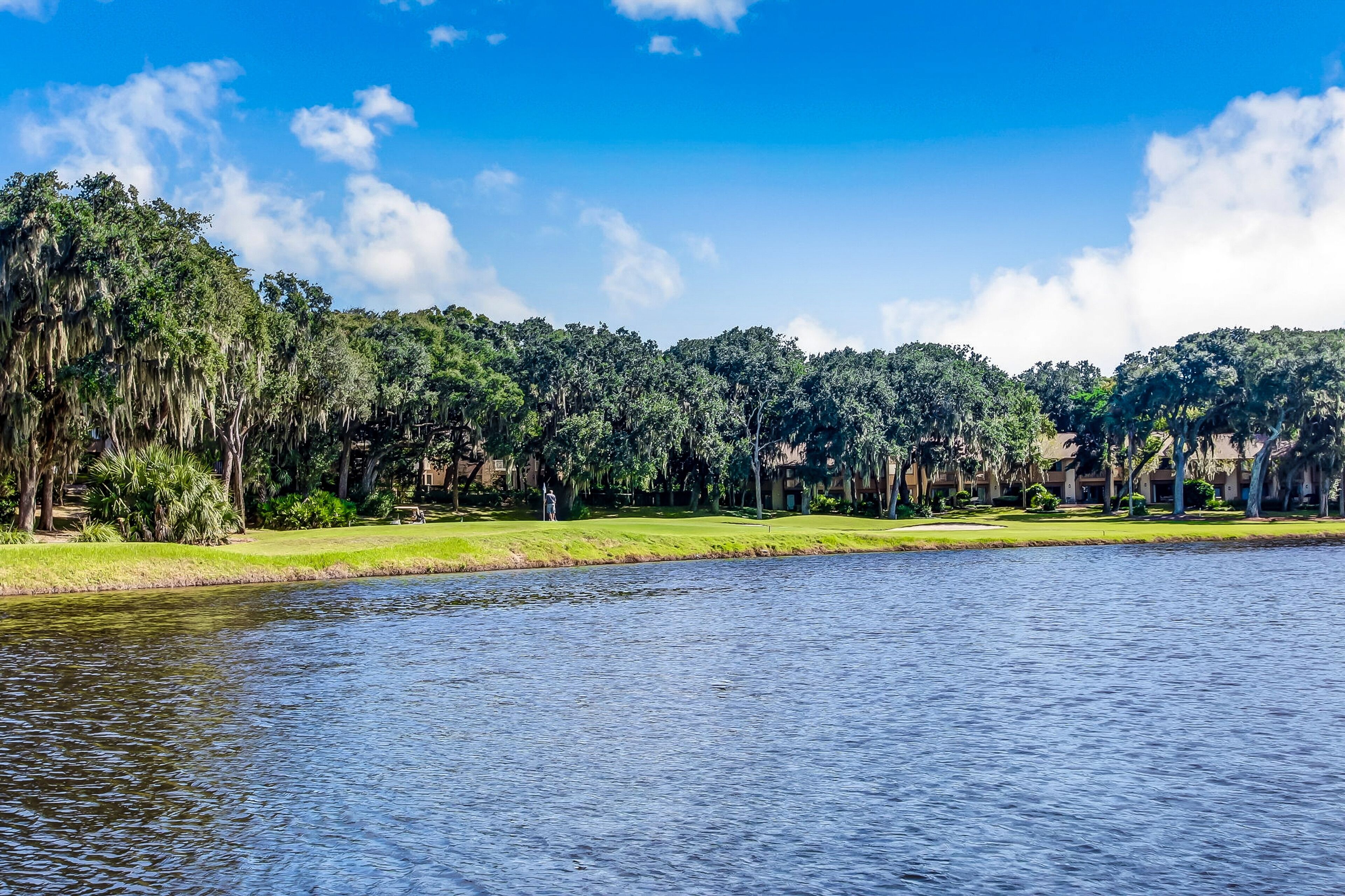 Blick auf einen See mit Golfplatz, Bäumen und einem Gebäudekomplex.