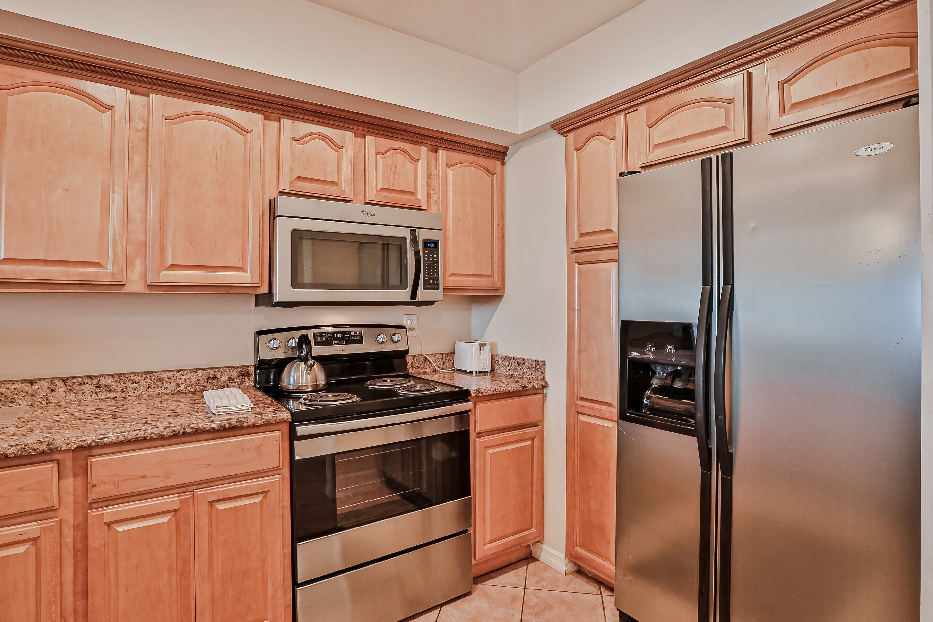 A kitchen with wooden cabinets, a stainless steel refrigerator, a microwave, a stove, and a toaster.