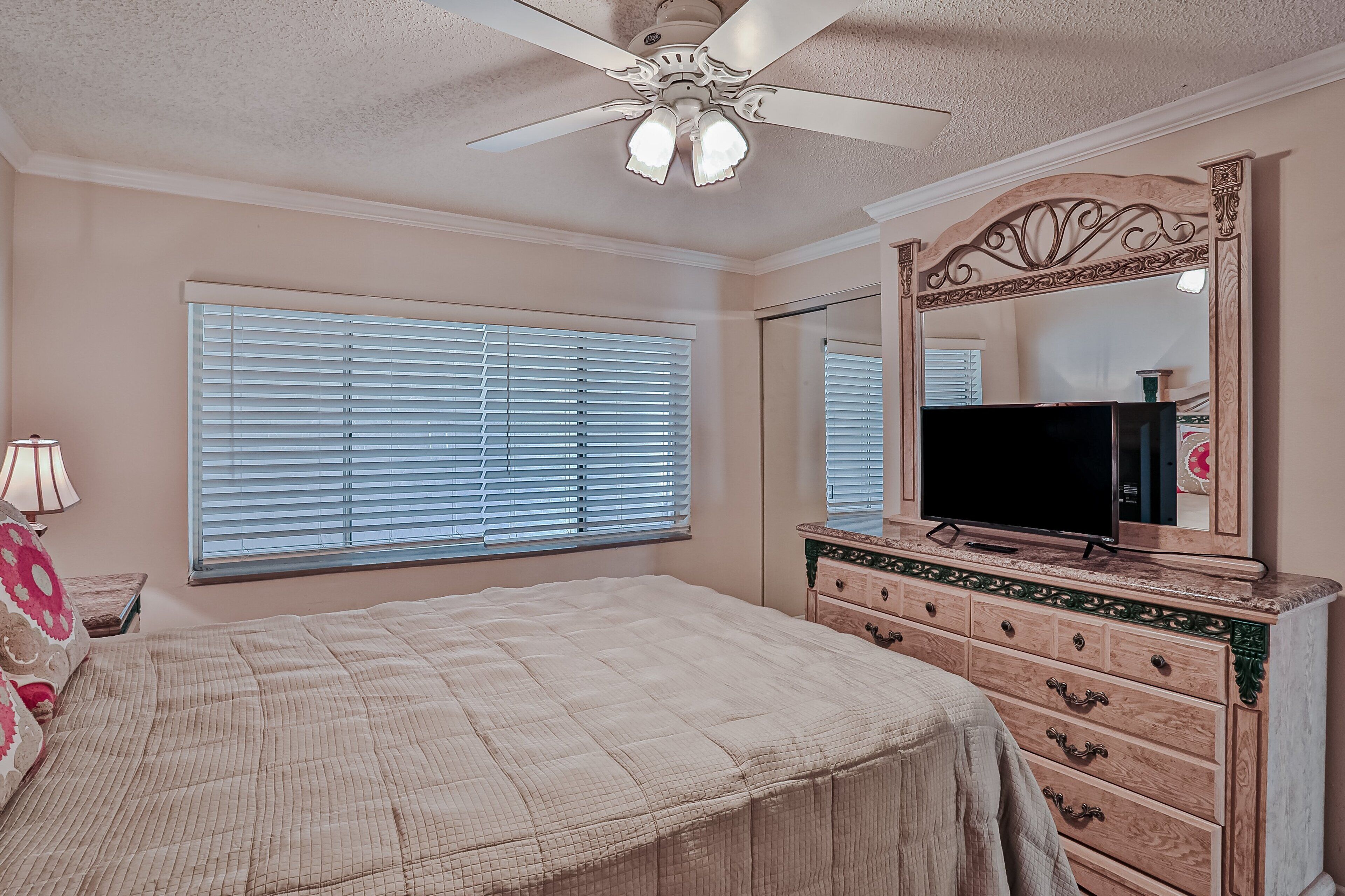 Ein Schlafzimmer mit Bett, Kommode, Spiegel, Deckenventilator und Fensterläden.