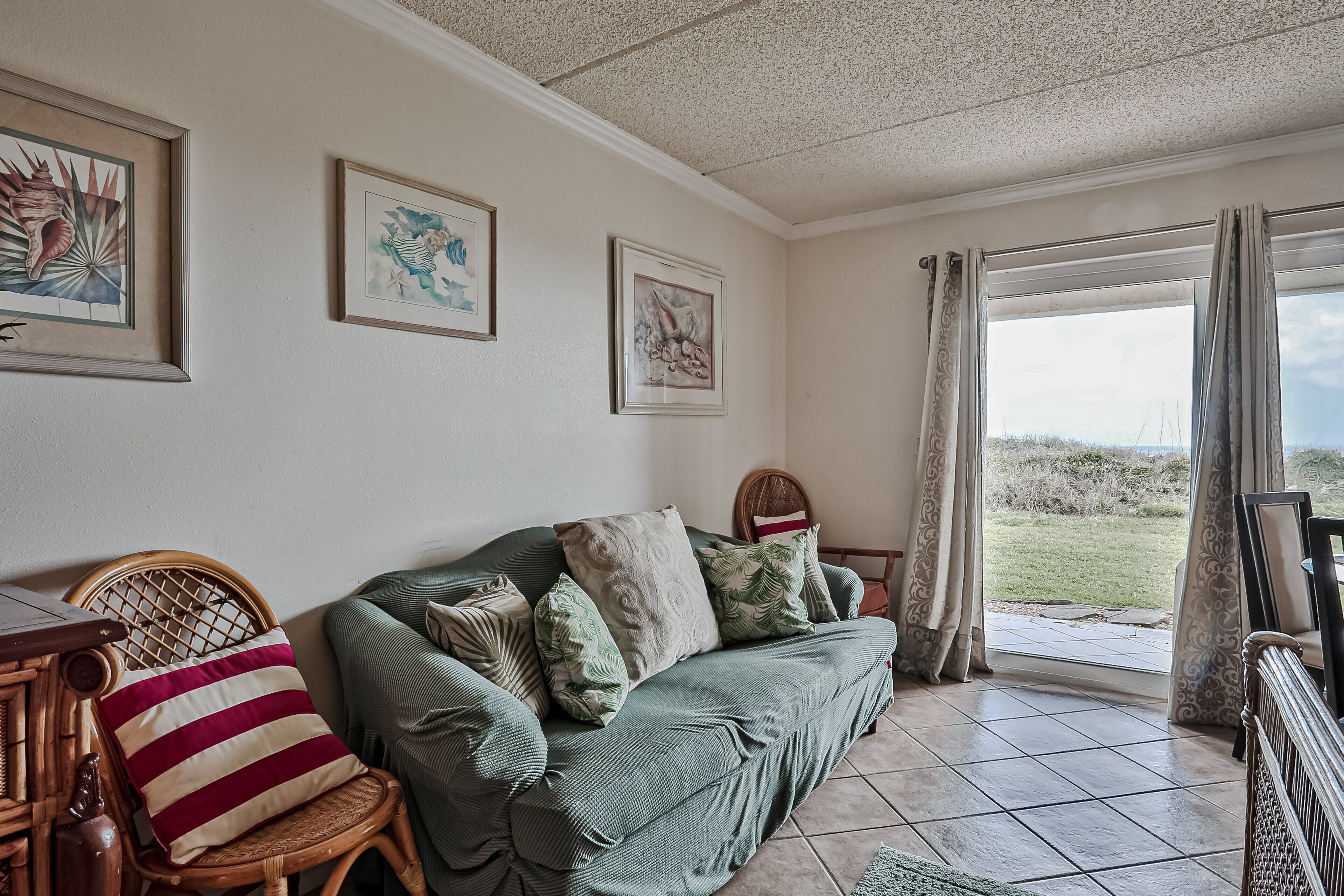 Een gezellige woonkamer met een groene bank, rieten stoelen en uitzicht door een groot raam.