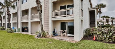 A multi-story residential building with balconies, a grassy lawn, and palm trees.