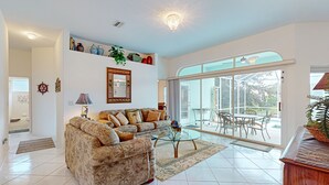 A spacious living room with a sofa, a glass coffee table, and a view of the outdoor patio. - Prime House With Lanai, Private Pool, Bbq, and Water Views (Palm Coast)