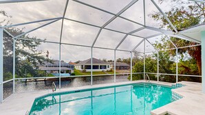 A swimming pool with a glass enclosure, a clear view of houses and greenery in the background, and a calm water surface. - Prime House With Lanai, Private Pool, Bbq, and Water Views (Palm Coast)