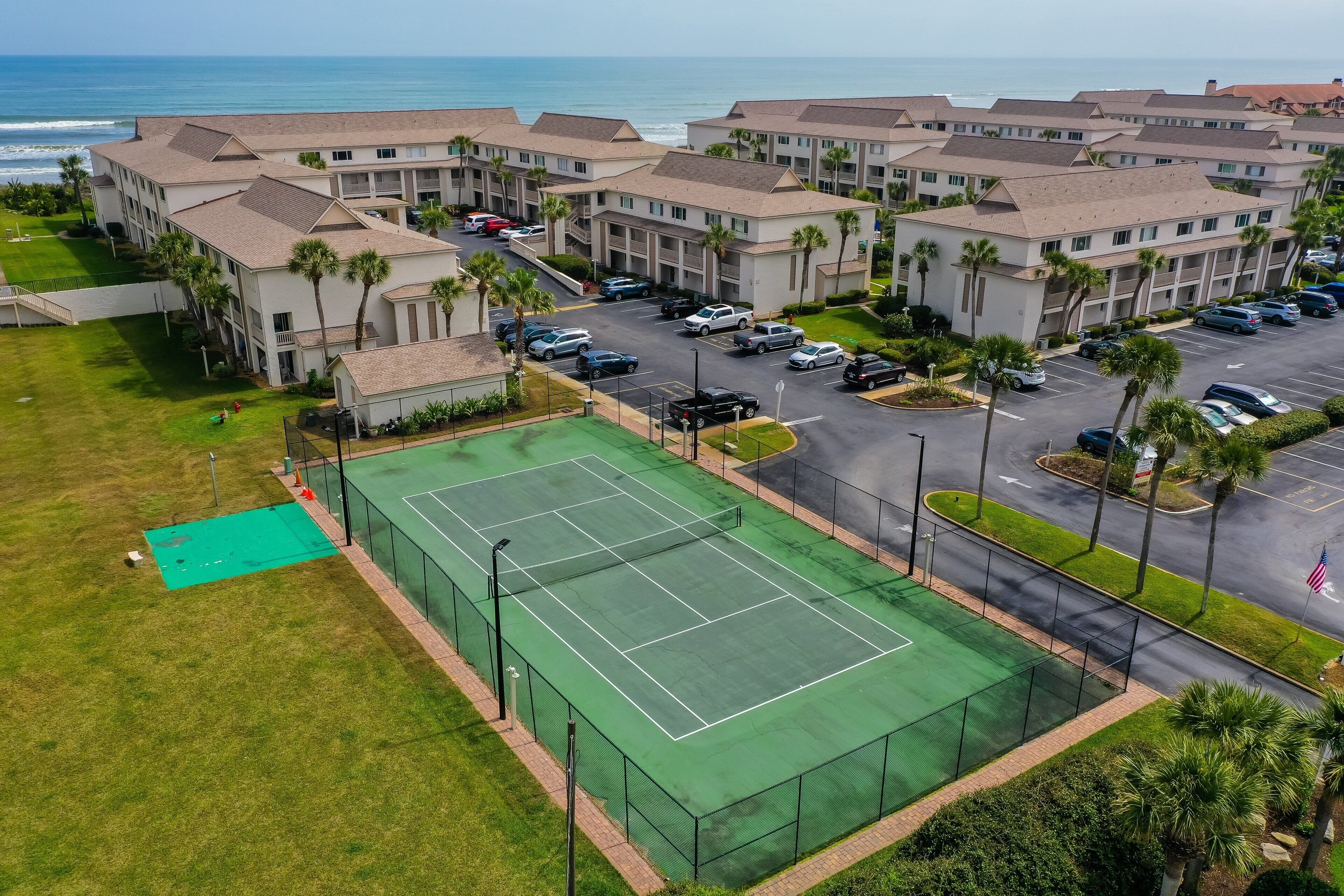 Un hotel de varios pisos con cancha de tenis, estacionamiento y vista al océano.