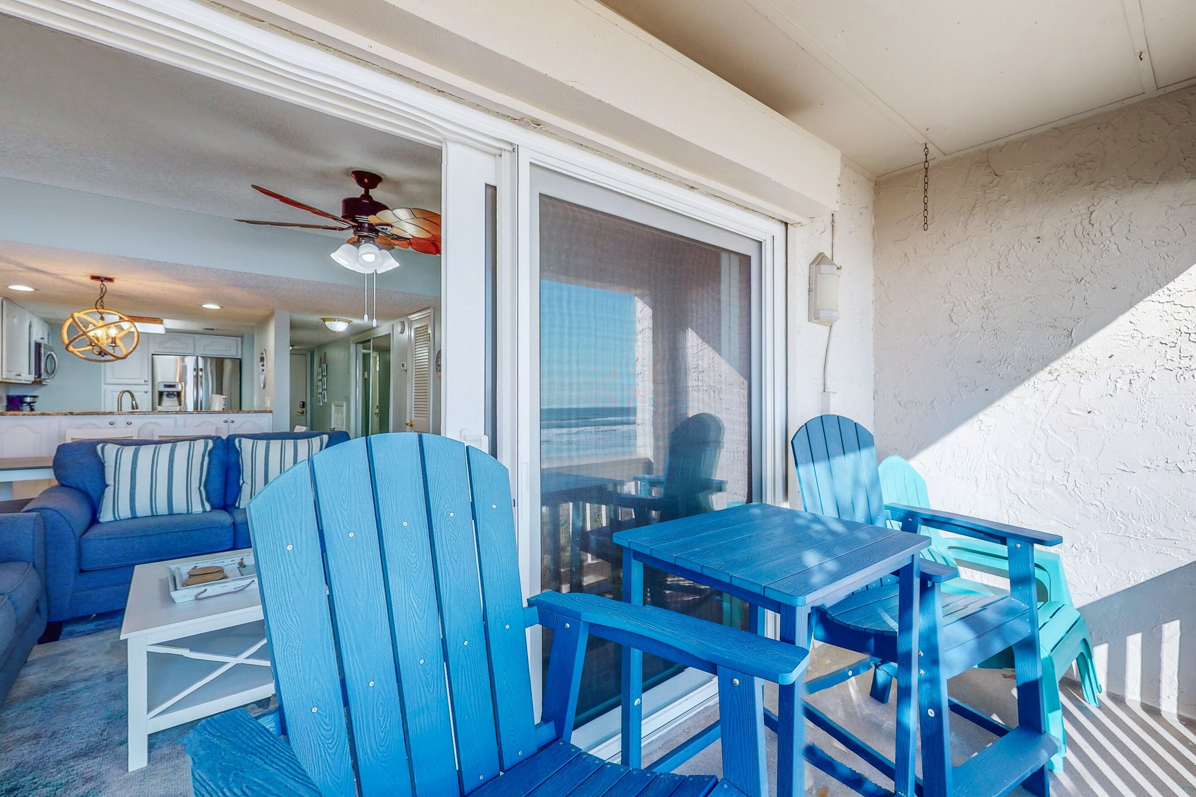 A blue-themed outdoor seating area with a table and chairs, a ceiling fan, and a view of the interior through a sliding glass door.