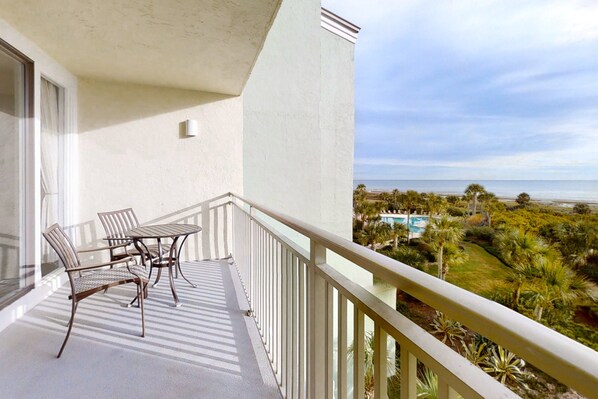 A balcony with a table and chairs, overlooking a pool and a coastal landscape. - Oceanfront Condo With Large Balcony, Pool, Central AC & Views (Fernandina Beach)