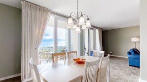 A dining area with a white table and chairs, a chandelier, and large windows with curtains. - Oceanfront Condo With Large Balcony, Pool, Central AC & Views (Fernandina Beach)
