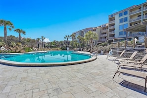 A swimming pool with lounge chairs and a building with balconies in the background. - Oceanfront Condo With Large Balcony, Pool, Central AC & Views (Fernandina Beach)