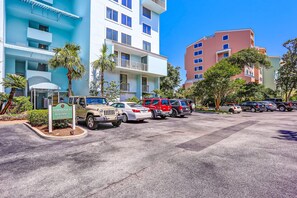 A parking lot with several cars, a sign for Shipwatch Building D, and a multi-story building with balconies and palm trees. - Oceanfront Condo With Large Balcony, Pool, Central AC & Views (Fernandina Beach)