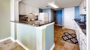 A kitchen with white cabinets, a granite countertop, and a patterned rug. - Oceanfront Condo With Large Balcony, Pool, Central AC & Views (Fernandina Beach)