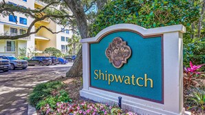 A sign with the name 'Shipwatch' surrounded by greenery and a parking area with cars. - Oceanfront Condo With Large Balcony, Pool, Central AC & Views (Fernandina Beach)