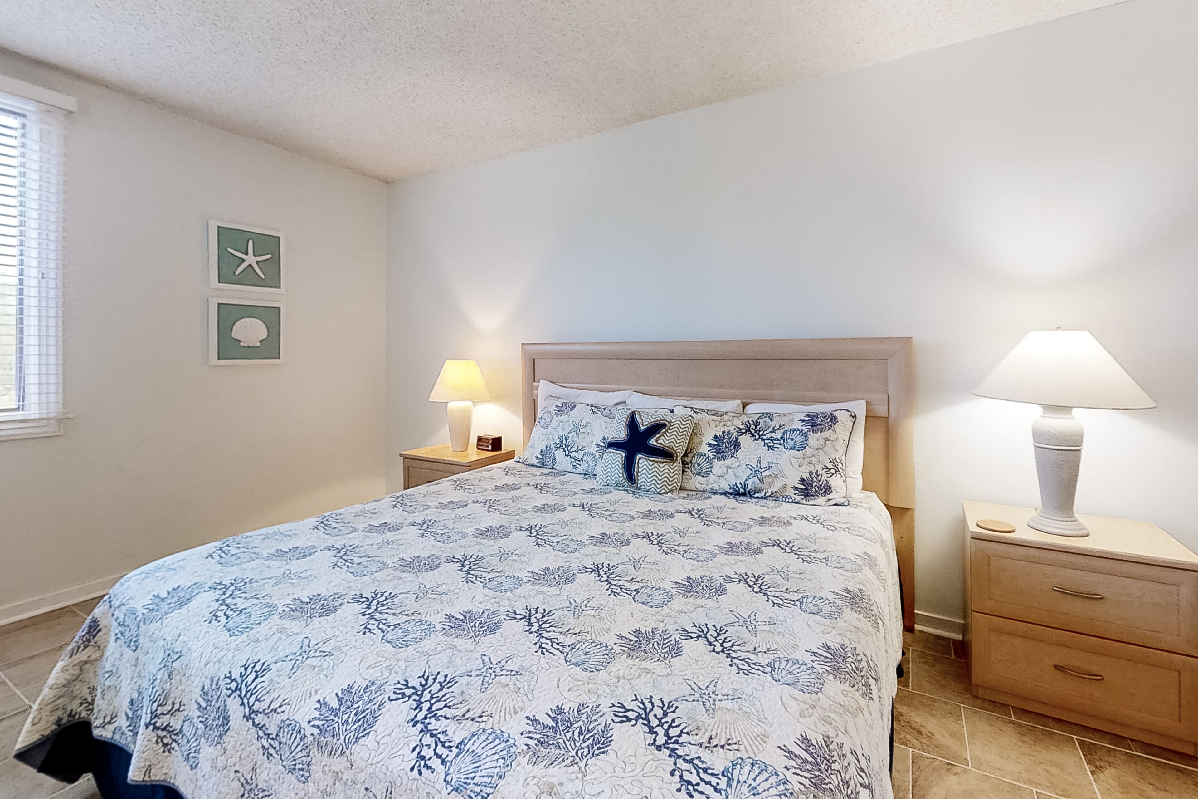 Une chambre à coucher comprenant un lit, deux tables de chevet, une commode, une lampe et des œuvres d’art murales.