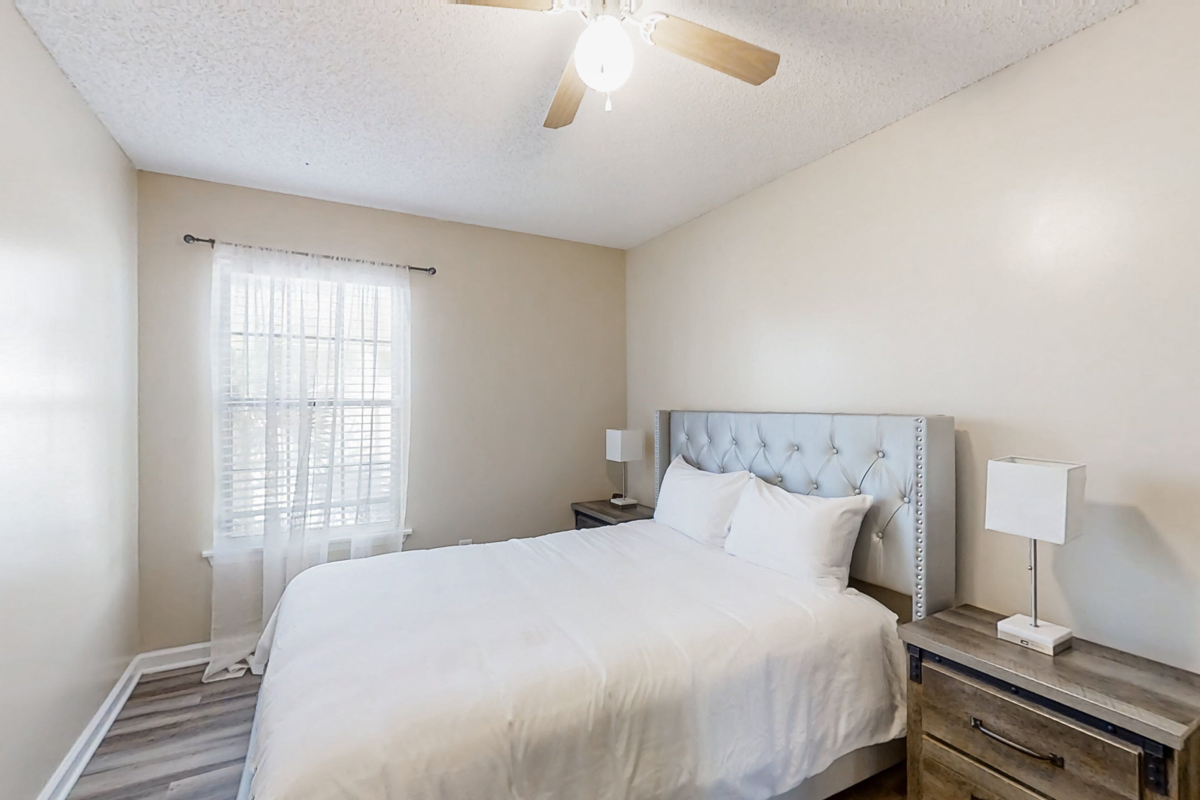 A bedroom with a bed, nightstands, a ceiling fan, and a window with blinds.