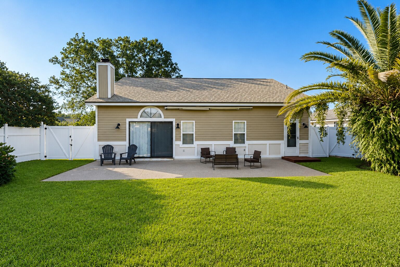 A single-story house with a covered patio, a white fence, and a palm tree.