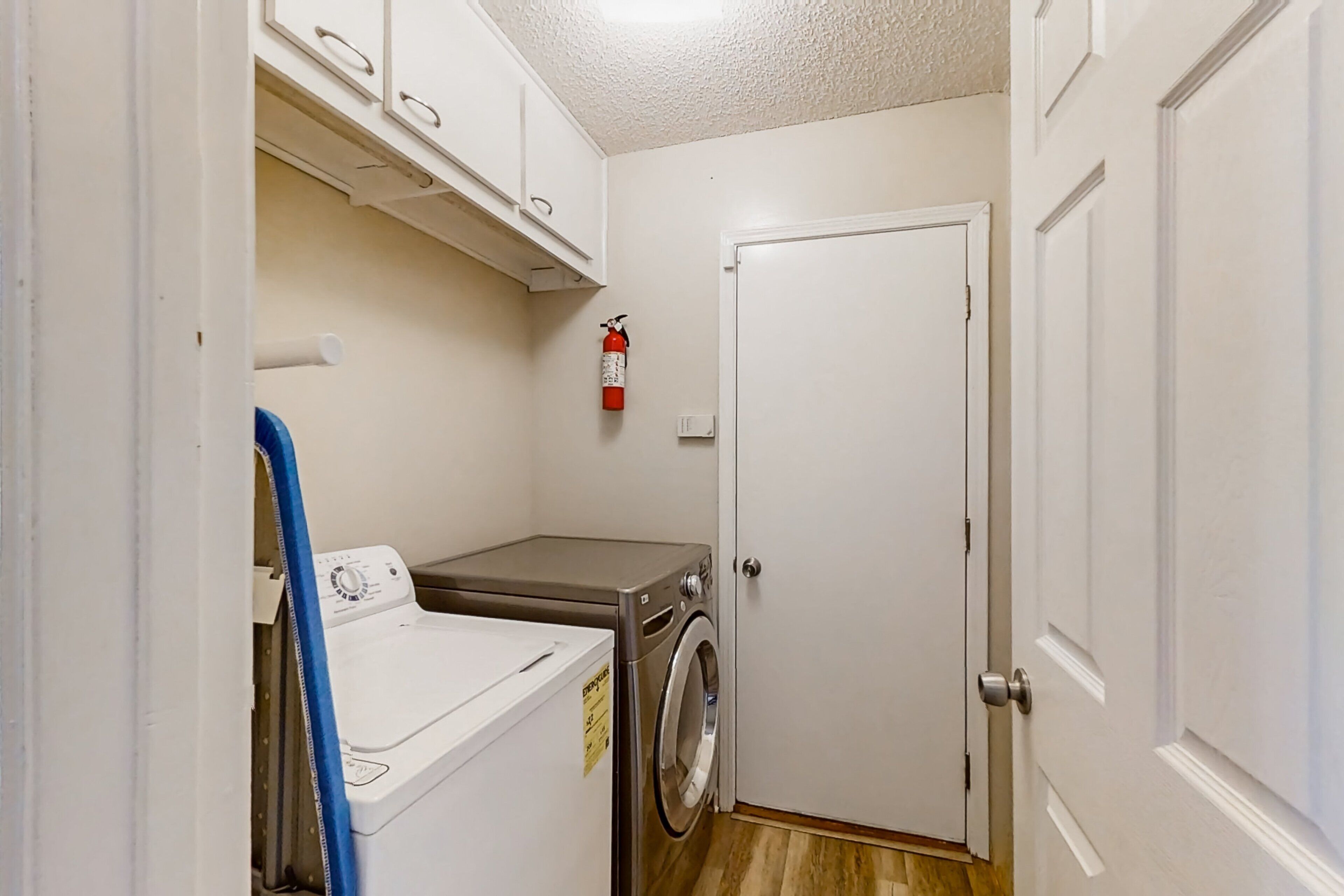A laundry room with a washing machine and dryer, a fire extinguisher, and a door.