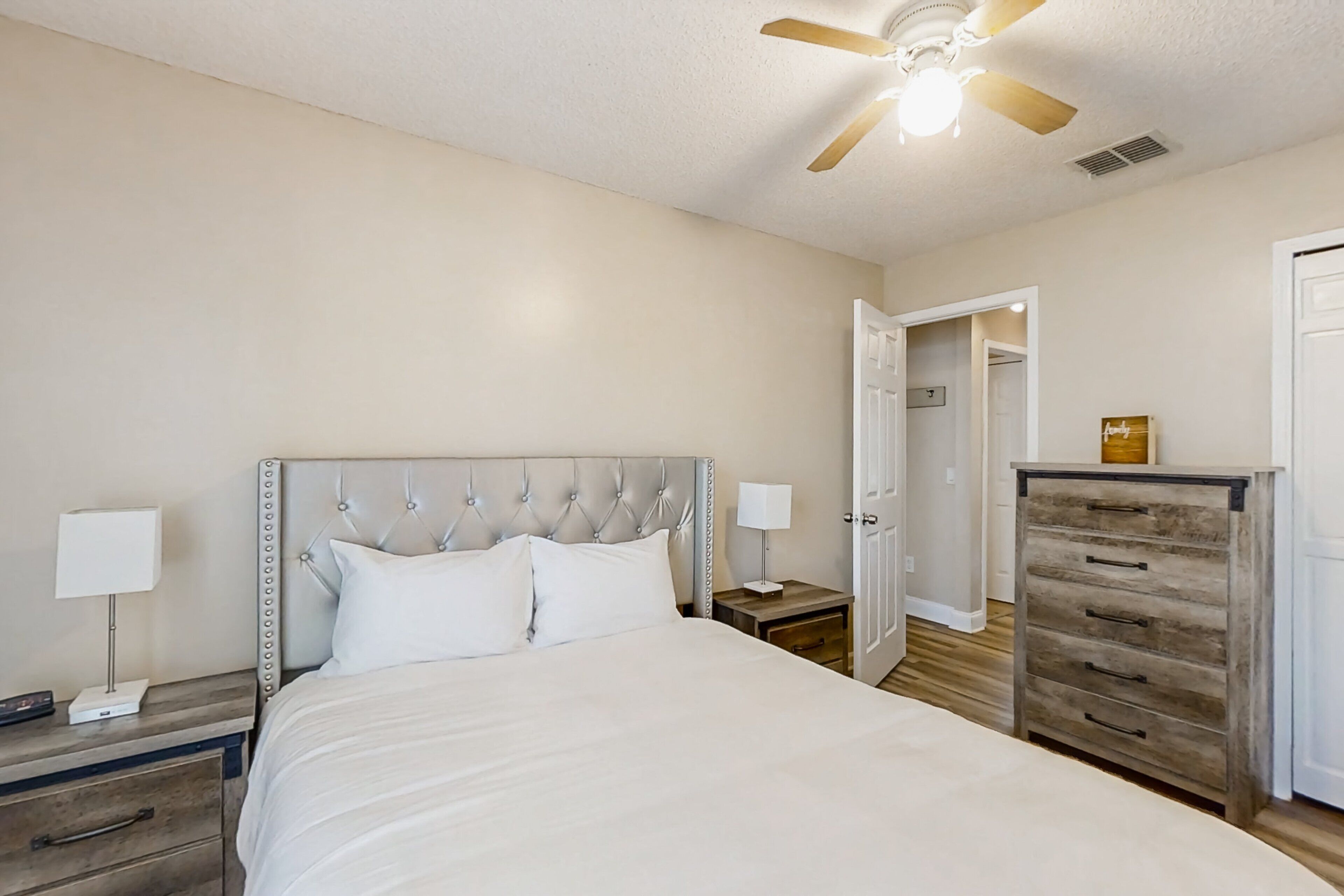 Une chambre à coucher avec un grand lit, deux tables de chevet, un ventilateur de plafond et une commode en bois.