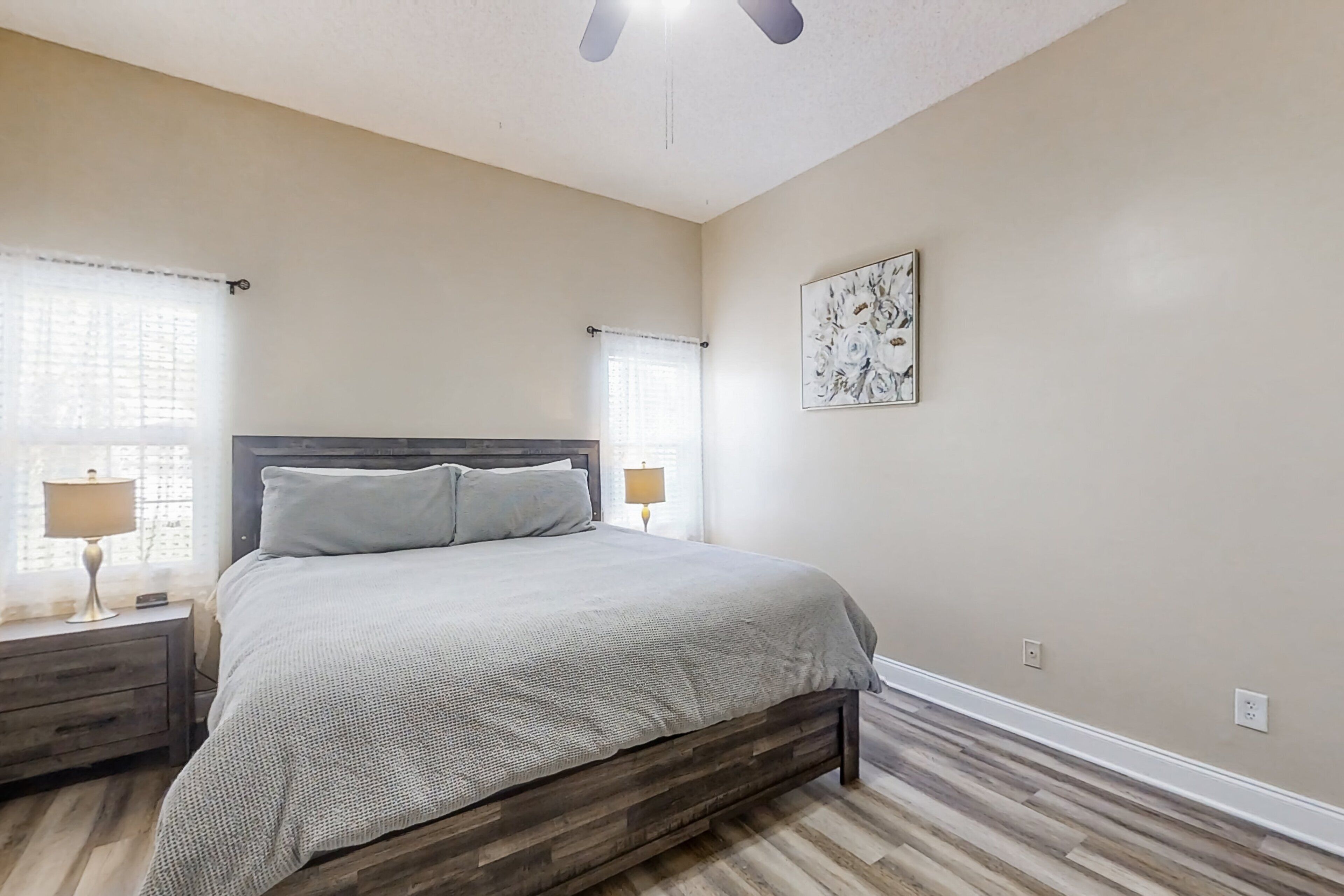 A bedroom with a bed, nightstands, a ceiling fan, and a window with curtains.