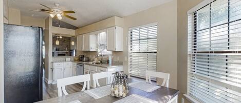 A modern kitchen with white cabinets, a black refrigerator, and a dining area with a wooden table and chairs.