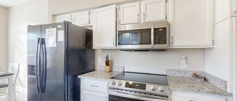 Una cocina moderna con armarios blancos, un refrigerador negro, un microondas y una estufa.