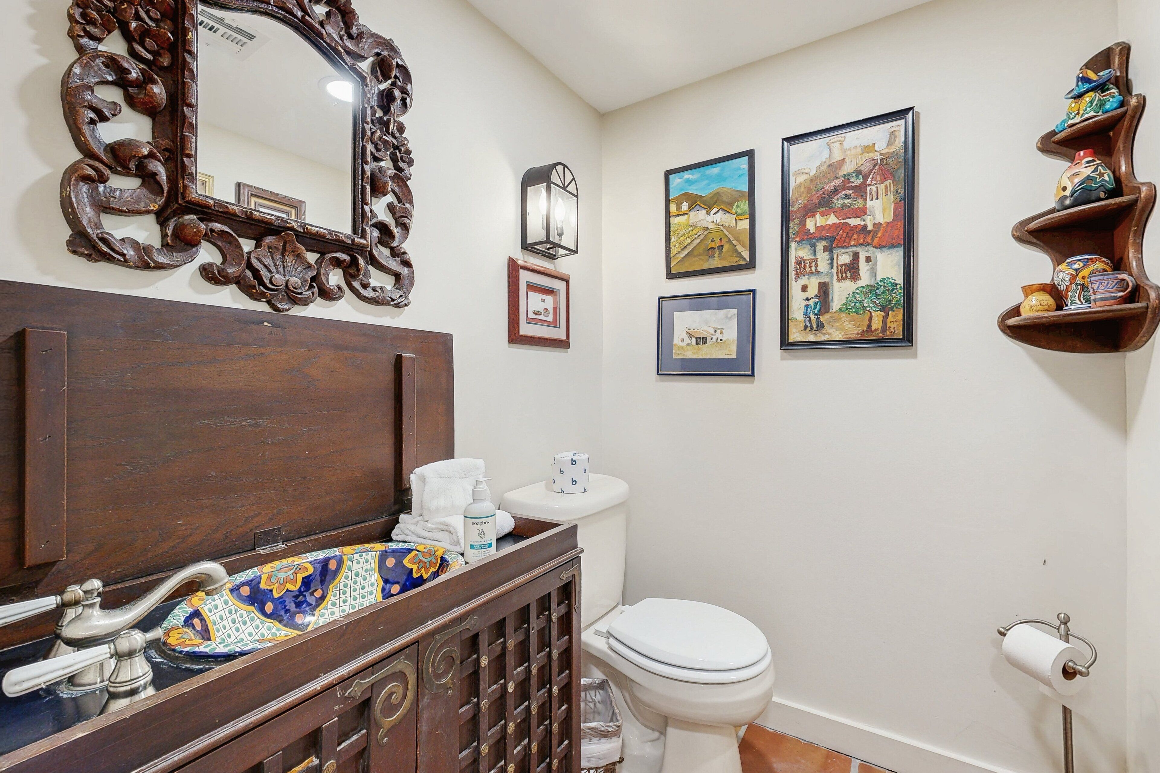 A bathroom with a wooden vanity, a mirror, a toilet, and a shelf with decorative items.