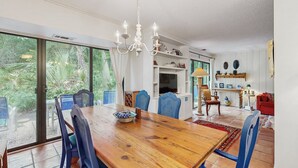 A dining area with a wooden table and blue chairs, a chandelier, and a view of greenery through large sliding glass doors. - Spacious 3br/3ba Dog-friendly Condo With Pool - Fernandina Beach Access (Fernandina Beach)